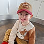 toddler, child, cap, sweater, fox_design, red_socks, pants, floor, kitchen, cabinet, smile, sitting, cute, indoors, portrait, happy, young_child, clothing, person, casual_wear