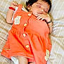 Ibadat is registered to the contest to win money with this photo: baby, sleeping, orange_dress, infant, cute, bed, striped_bedspread, peaceful, child, adorable, clothing, patches, hand, bracelet, soft, resting, small, cute_outfit, lying_down, cozy