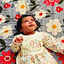 Ibadat is registered to the contest to win money with this photo: baby, infant, child, lying_down, floral_blanket, colorful, cute, curious_expression, clothing, penguin_pattern, soft_lighting, indoors, portrait, smiling, young_child, playful, fabric, patterned, head, face