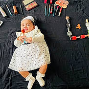 Ibadat joined the competition — help win amazing prizes! baby, child, makeup, cosmetics, nail_polish, brush, white_dress, headband, black_background, smiling, lying_down, colorful, playful, cute, infant, beauty, face, hands, socks, number_four