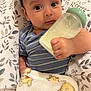 Luca is registered to the contest to win money with this photo: baby, milk_bottle, blanket, cushion, leaf_pattern, striped_clothing, infant, hand, face, eyes, portrait, indoor, soft_texture, feeding, cute, child, sleeping_area, comfort, rest, baby_garment