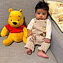 baby, child, plush_toy, winnie_the_pooh, couch, blanket, indoor, cute, infant, clothing, soft_toy, portrait, seated, happy, smile, hand, foot, fabric, furniture, person