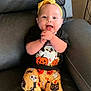 baby, child, smiling, happy, sitting, couch, clothing, headband, halloween, pumpkin, ghost, bat, spider, face, person, indoor, cute, pants, black_shirt, yellow