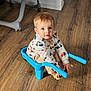 toddler, child, blue_chair, sitting, wooden_floor, sweatshirt, trucks, beige_pants, indoor, flooring, curious, looking_at_camera, small_chair, plastic_chair, light_brown_hair, long_sleeves, casual_clothing, baby, person, home