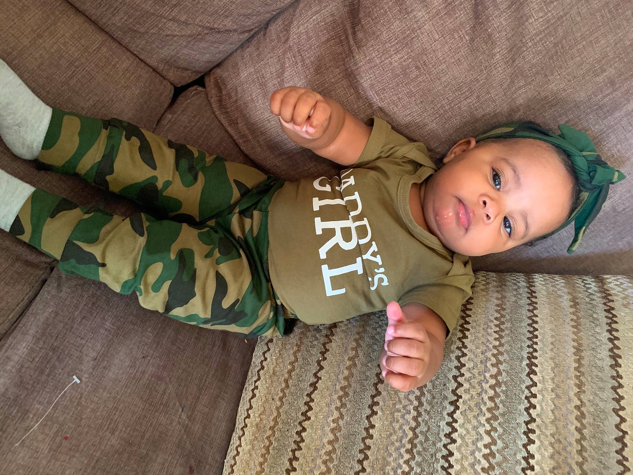 Jamayah is registered to the contest to win money with this photo: arm, baby, baby_products, baby_toddler_clothing, bedtime, camouflage, cheek, child, comfort, finger, flooring, linens, military_camouflage, pattern, person, sitting, skin, sleeve, textile, toddler