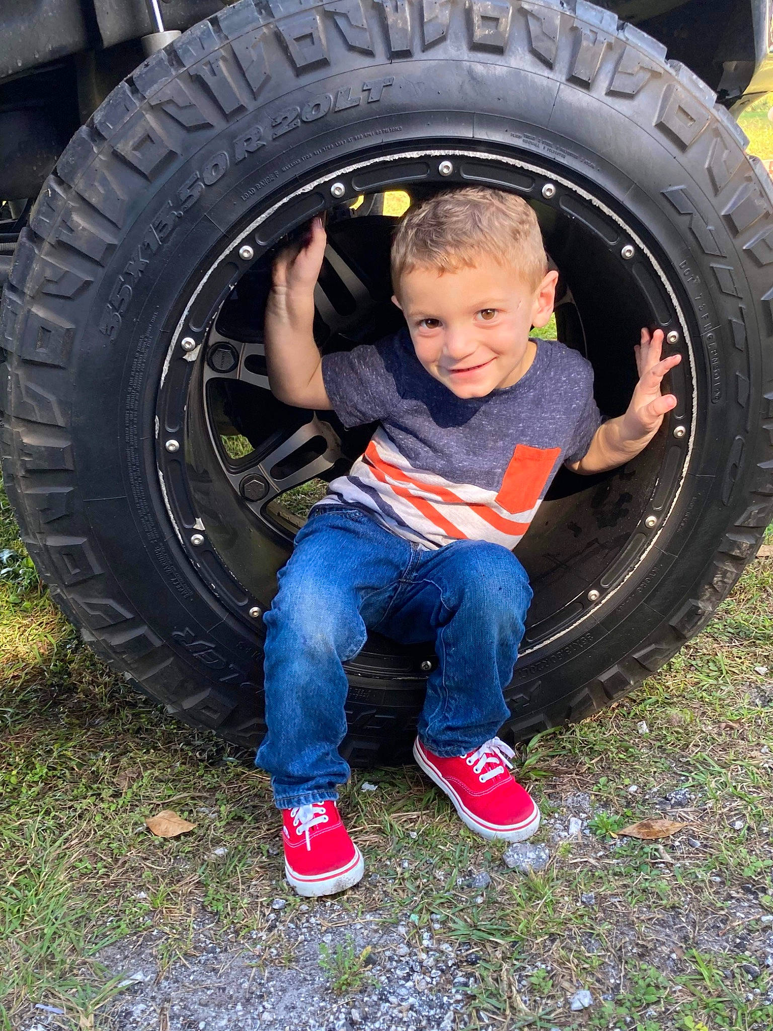 Elliot is registered to the contest to win money with this photo: alloy_wheel, automotive_design, automotive_exterior, automotive_tire, bumper, car, fender, grass, hubcap, joy, locking_hubs, motor_vehicle, person, rim, rolling, smile, sneakers, synthetic_rubber, tire, tread