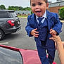 Kaiden is registered to the contest to win money with this photo: toddler, child, smiling, blue_suit, brown_loafers, car, red_car, parking_lot, adult_hand, outdoor, building, cloudy_sky, happy, portrait, person, fashion, formal_wear, vehicle, black_socks, holding