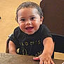 toddler, child, smiling, indoor, table, black_shirt, curly_hair, happy, face, hand, person, furniture, wood, seated, young_child, cute, portrait, bright_eyes, candid, casual