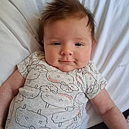 Zoey is registered to the contest to win money with this photo: baby, infant, cute, smile, face, hair, clothing, onesie, pattern, sheep, lying_down, blanket, white, skin, child, portrait, indoors, young, adorable, happy