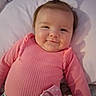 Zoey is registered to the contest to win money with this photo: baby, infant, pink_sweater, ponytail, pillow, pacifier, clip, smile, face, cheeks, lying_down, shadow, clothing, cute, child, indoor, person, portrait, happy, baby_girl