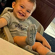 Maverick joined the competition — help win amazing prizes! toddler, child, baby, smiling, portrait, high_chair, sitting, indoors, face, hair, eyes, teeth, gray_shirt, socks, foot, legs, wooden_background, home, happy, photography