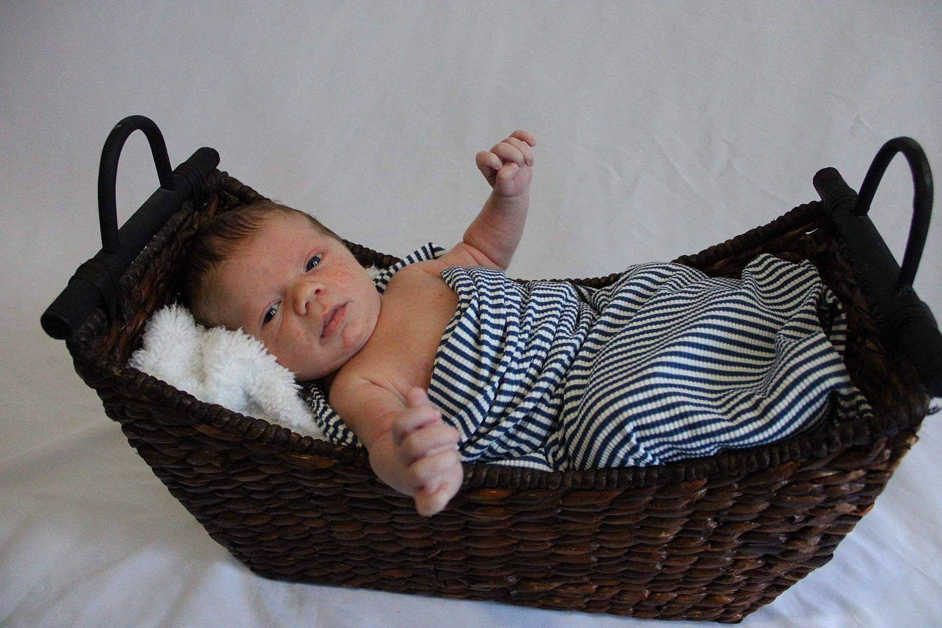 Cohen is registered to the contest to win money with this photo: baby, baby_products, baby_toddler_clothing, bag, basket, child, comfort, fashion_accessory, flash_photography, foot, grass, home_accessories, pattern, person, sitting, storage_basket, toddler, wicker, wood