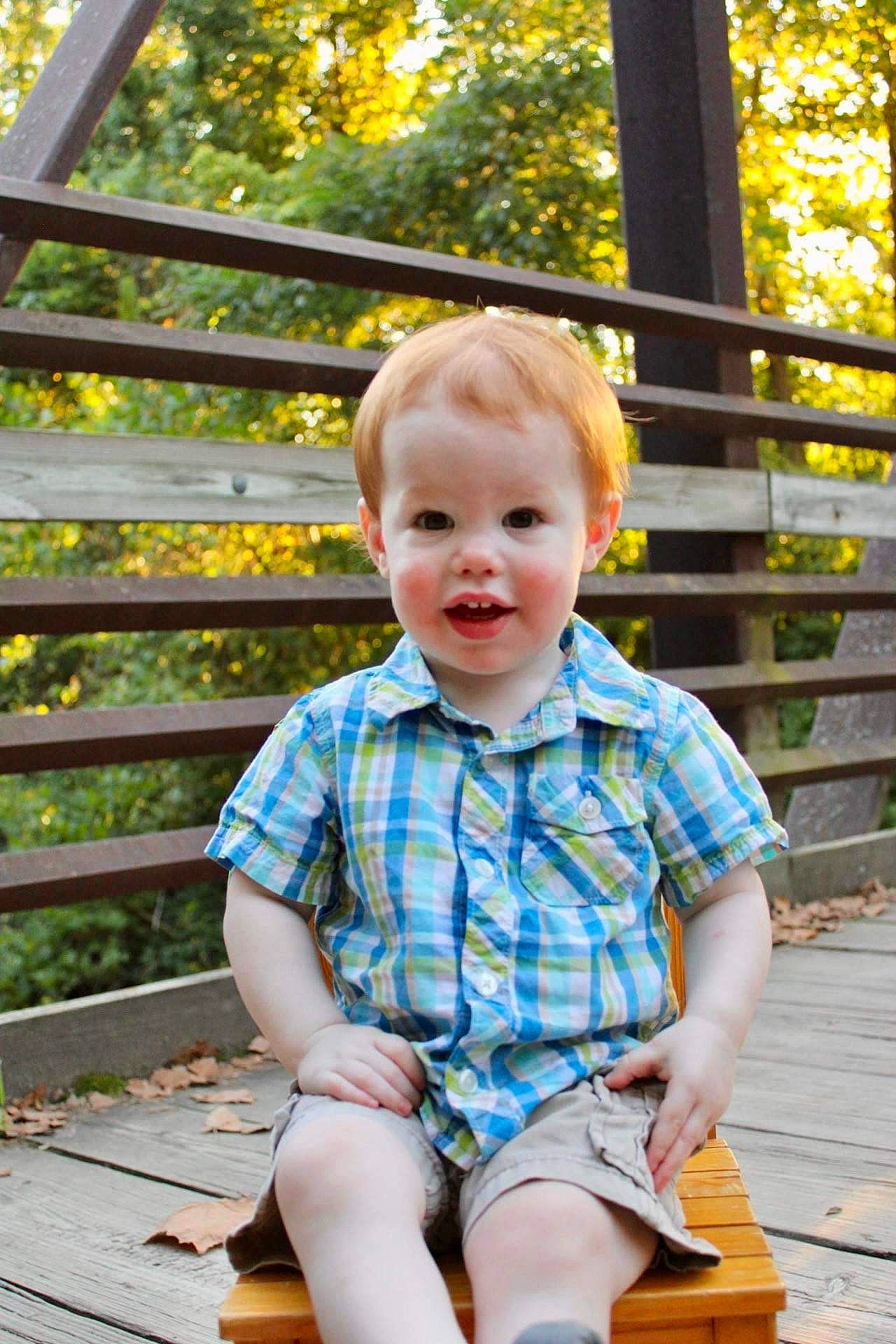 Everett is registered to the contest to win money with this photo: baby_toddler_clothing, child, eye, face, facial_expression, grass, happy, head, leaf, leisure, people_in_nature, person, plaid, shorts, smile, standing, summer, t_shirt, toddler, wood