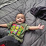baby, child, tshirt, green_tshirt, cartoon, ninja_turtles, bedspread, gray_bedspread, blanket, pillow, lying_down, smiling, arms_outstretched, indoors, cozy, clothing, person, cute, infant, happy