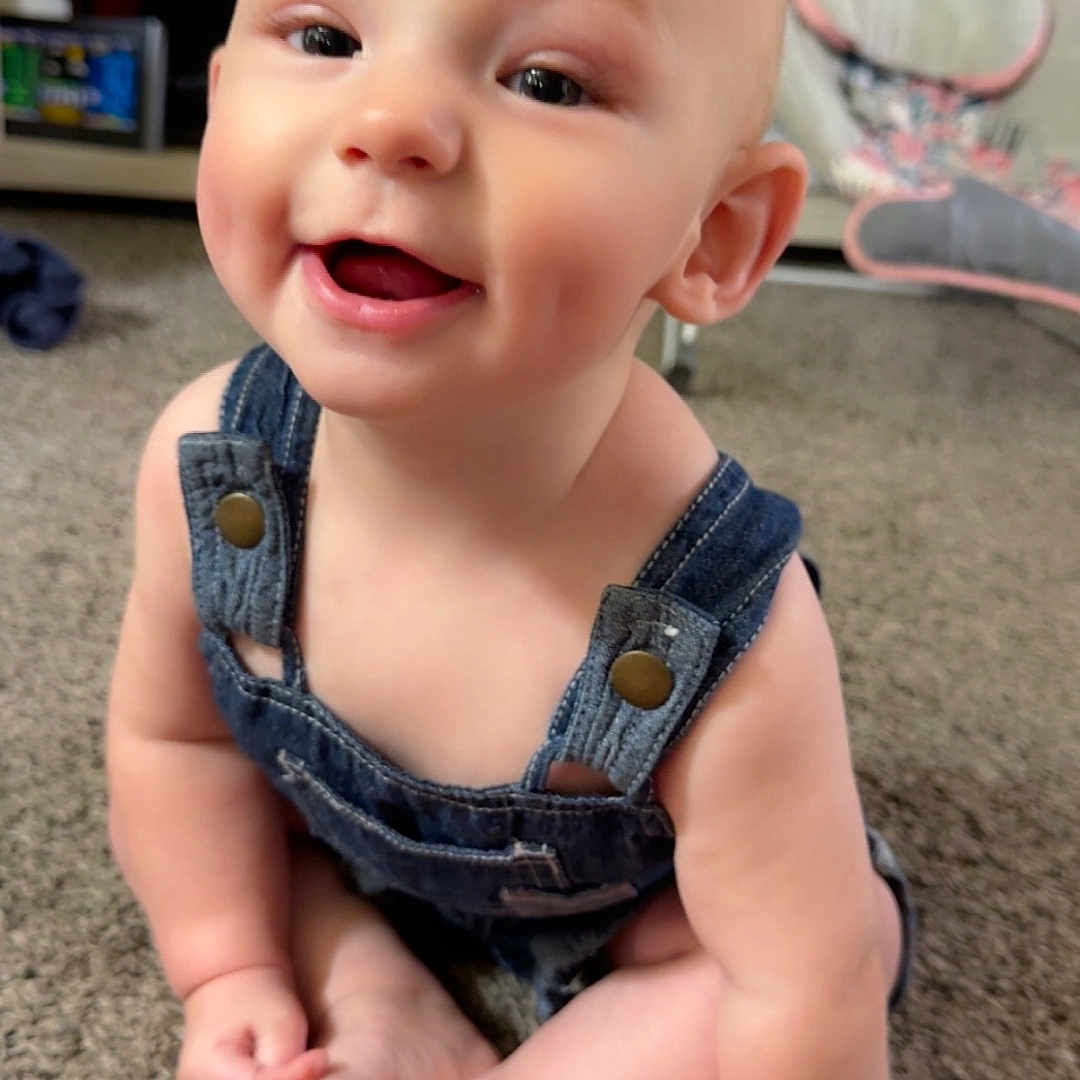 Attlee is registered to the contest to win money with this photo: baby, child, infant, denim_overalls, smile, happy, sitting, carpet, indoor, cute, face, skin, hand, foot, person, expression, young, home, furniture, toy