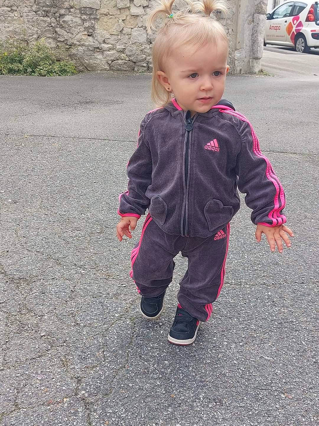 Léna participe au concours pour gagner de l'argent avec cette photo : asphalt, baby, baby_toddler_clothing, car, flooring, gesture, grass, head, leg, outerwear, pattern, people_in_nature, person, plant, road_surface, sleeve, tire, toddler, tree, walking