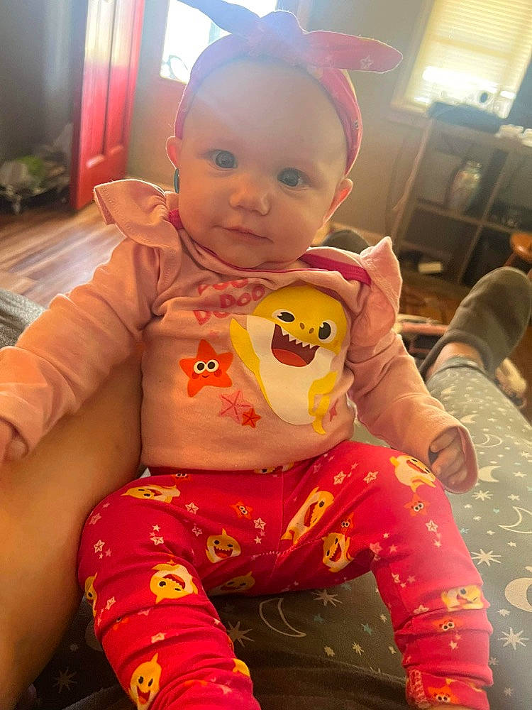 Katie is registered to the contest to win money with this photo: baby, baby_toddler_clothing, bib, carmine, cheek, child, costume, fictional_character, flooring, fun, happy, lap, mouth, person, pink, play, sitting, skin, stuffed_toy, t_shirt