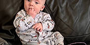 Elliott is registered to the contest to win money with this photo: baby, infant, mickey_mouse, onesie, clothing, couch, leather, fingers, hand, face, blue_eyes, sitting, indoor, wall, notebook, package, toy, person, child, casual