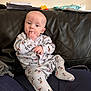 baby, infant, mickey_mouse, onesie, clothing, couch, leather, fingers, hand, face, blue_eyes, sitting, indoor, wall, notebook, package, toy, person, child, casual