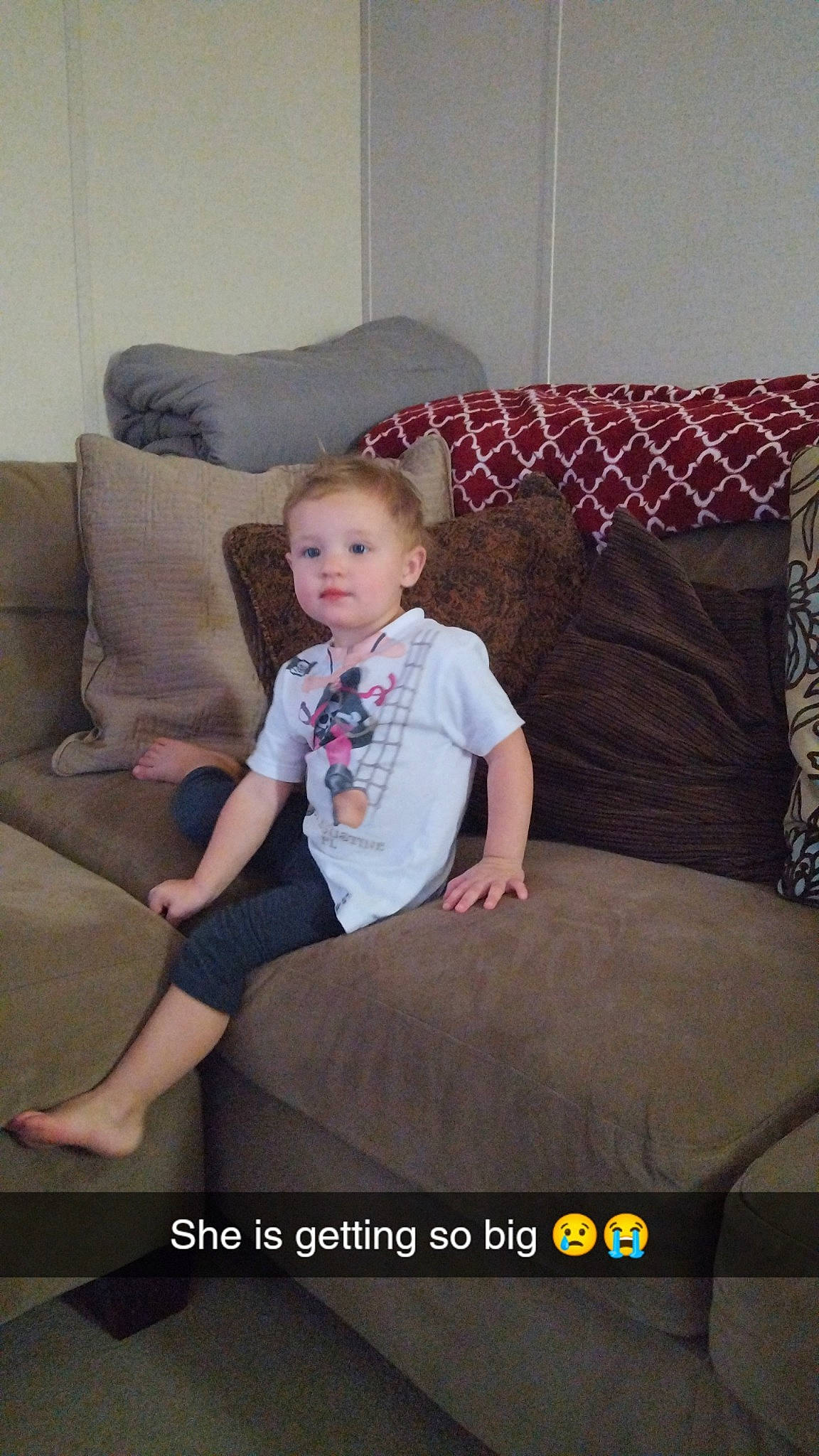 Lilly is registered to the contest to win money with this photo: child, comfort, couch, floor, flooring, fun, furniture, hardwood, human_leg, knee, living_room, magenta, mammal, person, room, t_shirt, textile, thigh, throw_pillow, toddler