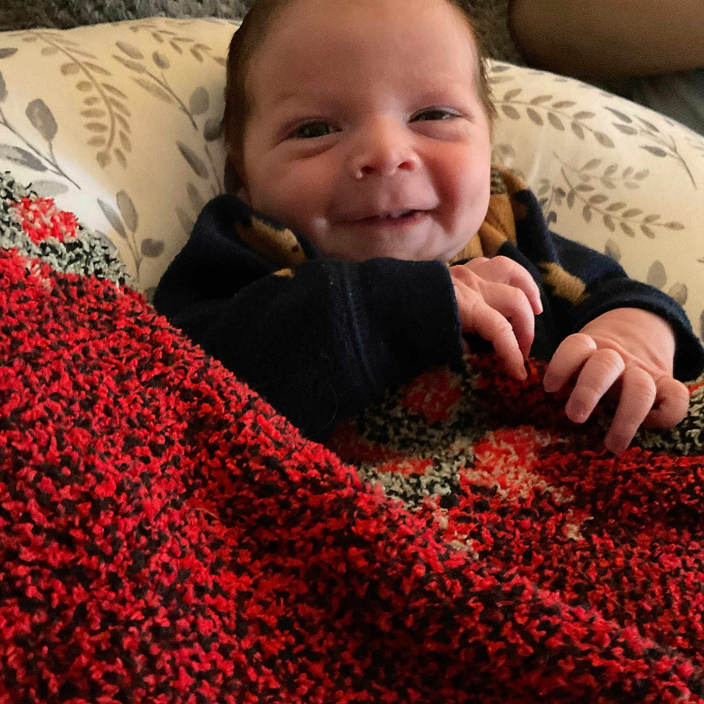 James Jr joined the competition — help win amazing prizes! arm, baby, black, blanket, closeup, cozy, cushion, face, hand, happy, indoor, infant, knitted, newborn, patterned, person, portrait, red, resting, smiling