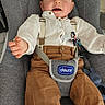 Maël a rejoint le concours — aidez-le/la à gagner de superbes lots ! baby, baby_seat, blue_bunny, brown_pants, child, clothing, comfortable, curious_expression, cute, gray_seat, indoor, infant, person, reaching_out, sitting, smiling, suspenders, toy, white_shirt, young_child
