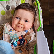 Maël participe au concours pour gagner de l'argent avec cette photo : baby, bib, blanket, blue, cheerful, child, clothing, cute, face, happy, head, high_chair, home, indoor, infant, person, seat, smiling, toy, young_child