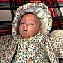 baby, blanket, button, child, cute, expression, fabric, face, floral_pattern, hooded_jacket, indoor, infant, lying_down, newborn, person, plaid, portrait, small_person, soft, warm_clothing