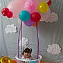 toddler, child, balloons, laundry_basket, birthday, party, decoration, cloud_cutouts, colorful, playful, indoor, celebration, headband, smiling, cute, pink, yellow, orange, purple, white
