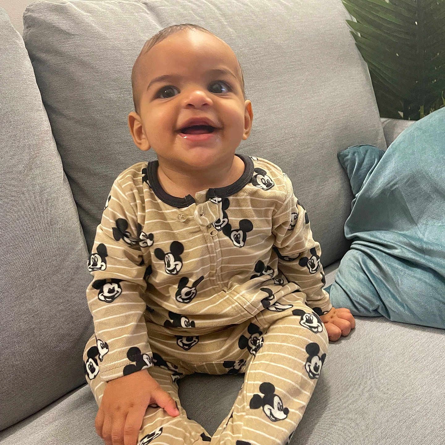 Mateys Aylan Evrard a rejoint le concours — aidez-le/la à gagner de superbes lots ! baby, blue_pillow, child, clothing, couch, cute, footed_pajamas, gray, happy, home, indoor, infant, mickey_mouse, pajamas, person, plant, portrait, seated, smiling, young_child