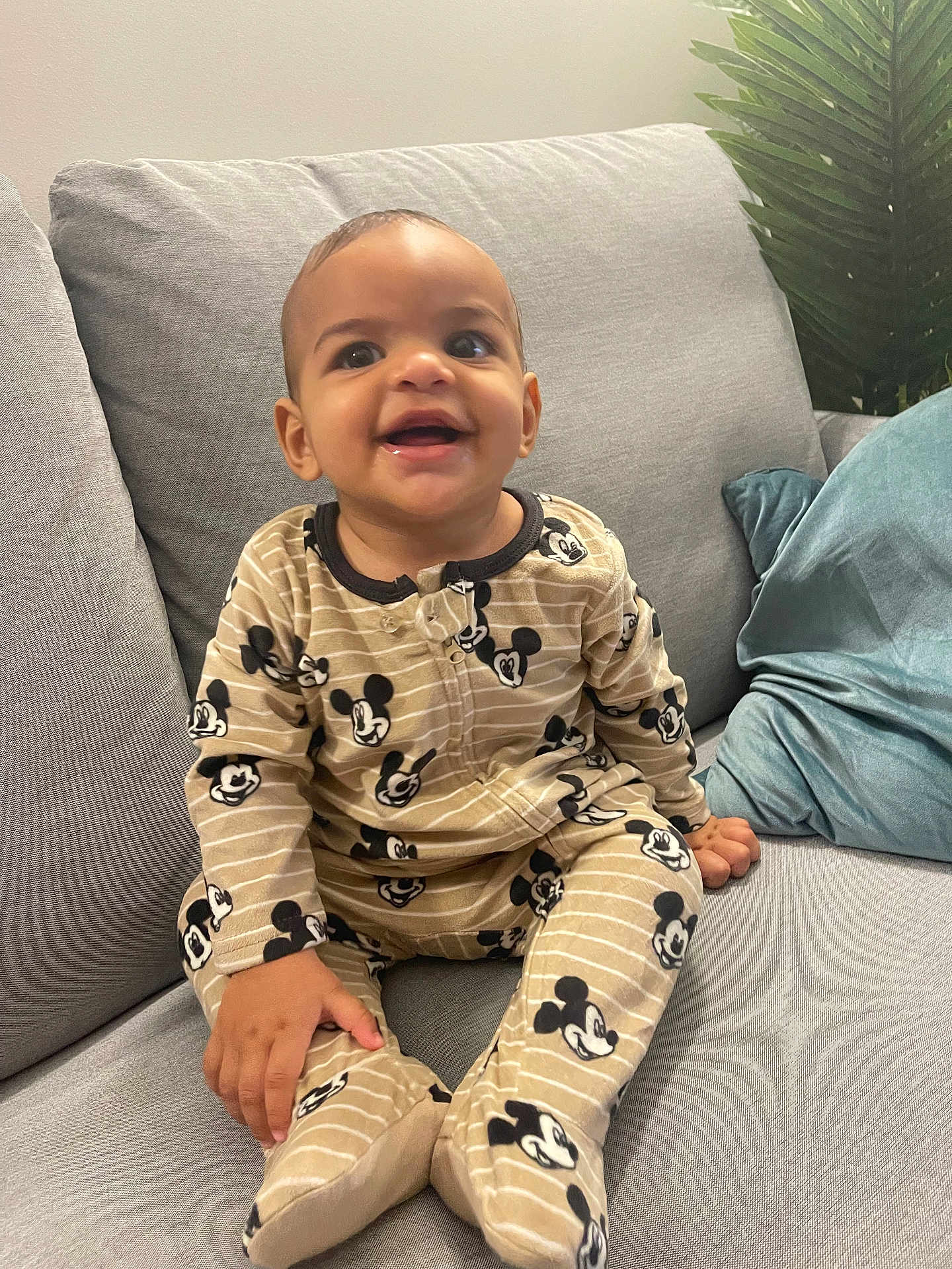 Mateys Aylan Evrard a rejoint le concours — aidez-le/la à gagner de superbes lots ! baby, child, smiling, mickey_mouse, pajamas, couch, gray, blue_pillow, plant, indoor, happy, seated, clothing, footed_pajamas, infant, person, cute, home, young_child, portrait