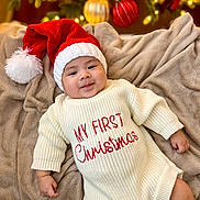 Dylan joined the competition — help win amazing prizes! baby, infant, santa_hat, christmas_sweater, blanket, holiday, festive, smiling, indoors, cozy, christmas_tree, ornament, red, white, warm_lighting, cute, portrait, celebration, seasonal, happy