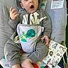 baby, baby_bouncer, child, comfort, cute, fabric, foot, grey_clothing, hand, hoodie, indoors, infant, nap, patterned, relaxed, seated, sleepy, toy_book, turtle_print, yawning