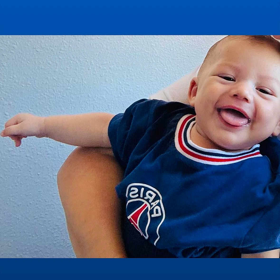 Liam-Noha Chalaye a rejoint le concours — aidez-le/la à gagner de superbes lots ! arm, baby, blue_shirt, casual_clothing, child, cute, hand, happy, holding, human, indoor, infant, paris_logo, person, portrait, smiling, texture, tongue_out, wall, young_child