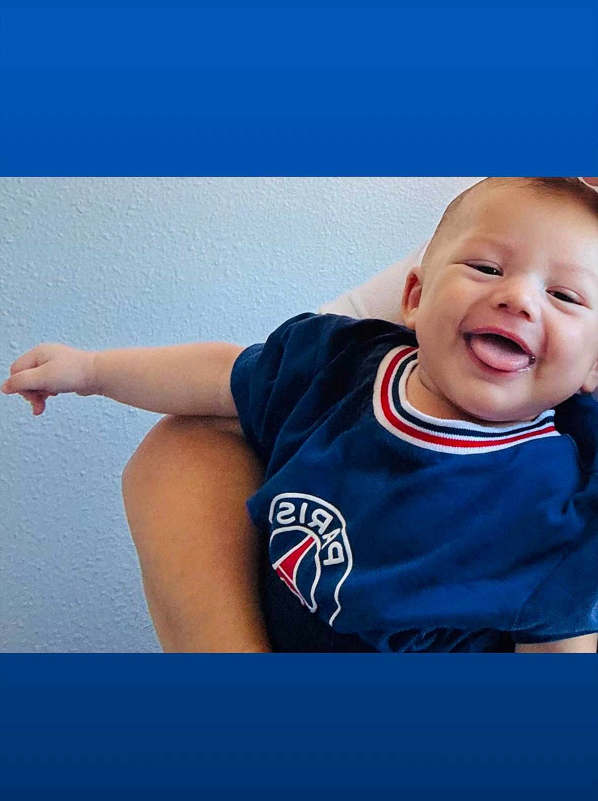 Liam-Noha Chalaye a rejoint le concours — aidez-le/la à gagner de superbes lots ! baby, child, smiling, tongue_out, blue_shirt, paris_logo, arm, hand, person, holding, happy, indoor, wall, texture, casual_clothing, portrait, cute, infant, young_child, human
