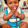 baby, child, infant, curly_hair, blue_onesie, bib, pacifier, bed, room, clothing, smiling, sitting, cute, playful, indoor, toy, hand, feet, bracelet, home
