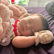 Milani joined the competition — help win amazing prizes! baby, sleeping, infant, bed, blanket, pink_blanket, purple_bedding, pacifier, red_bow, mitten, onesie, portrait, indoors, bedroom, resting, peaceful, face, closed_eyes, soft_toys, cozy