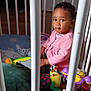 Nour participe au concours pour gagner de l'argent avec cette photo : toddler, child, playpen, toys, pink_jacket, indoor, flooring, stuffed_animal, colorful, curly_hair, baby, sitting, expression, playtime, plastic_toys, wood_floor, bars, young_child, cute, portrait