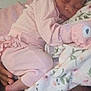 baby, sleeping, pink_clothing, hat, blanket, floral_pattern, infant, peaceful, soft_toys, hand, resting, closeup, portrait, cute, newborn, indoors, child, warm, comfort, tenderness