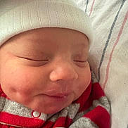 Elijah is registered to the contest to win money with this photo: baby, sleeping, hat, red_clothing, striped_clothing, blanket, closeup, face, newborn, soft_texture, peaceful, cute, infant, resting, dimples, warm, cozy, apparel, headwear, portrait