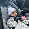baby, blanket, car_interior, car_seat, child, clothing, eyes, face, harness, hat, indoor, infant, looking_away, pink_toy, portrait, safe_travel, seatbelt, sitting, striped_hat, vehicle