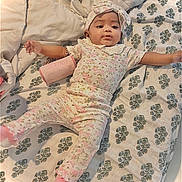 Nessa is registered to the contest to win money with this photo: arms_outstretched, baby, bed, bedroom, bedspread, bottle, bow, child, cute, floral_pattern, headband, indoor, infant, juicy, lying_down, pajamas, pink_clothing, portrait, smiling, socks