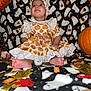 baby, child, halloween, pumpkin, dress, headband, blanket, ghost_pattern, autumn_leaves, orange, black, white, festive, holiday, cute, smiling, sitting, indoor, portrait, foot