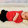 baby, infant, child, red_shirt, striped_shirt, black_shorts, lying_down, pillow, floral_pillow, indoor, crib, blanket, face, skin, feet, arms, expression, cute, young, resting