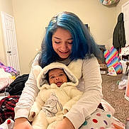 Ki'Mani is registered to the contest to win money with this photo: baby, child, woman, blue_hair, smiling, cozy_clothing, blanket, indoor, carpet, bedroom, happy, affection, family, hooded_outfit, casual, colorful, polka_dot, person, portrait, cute