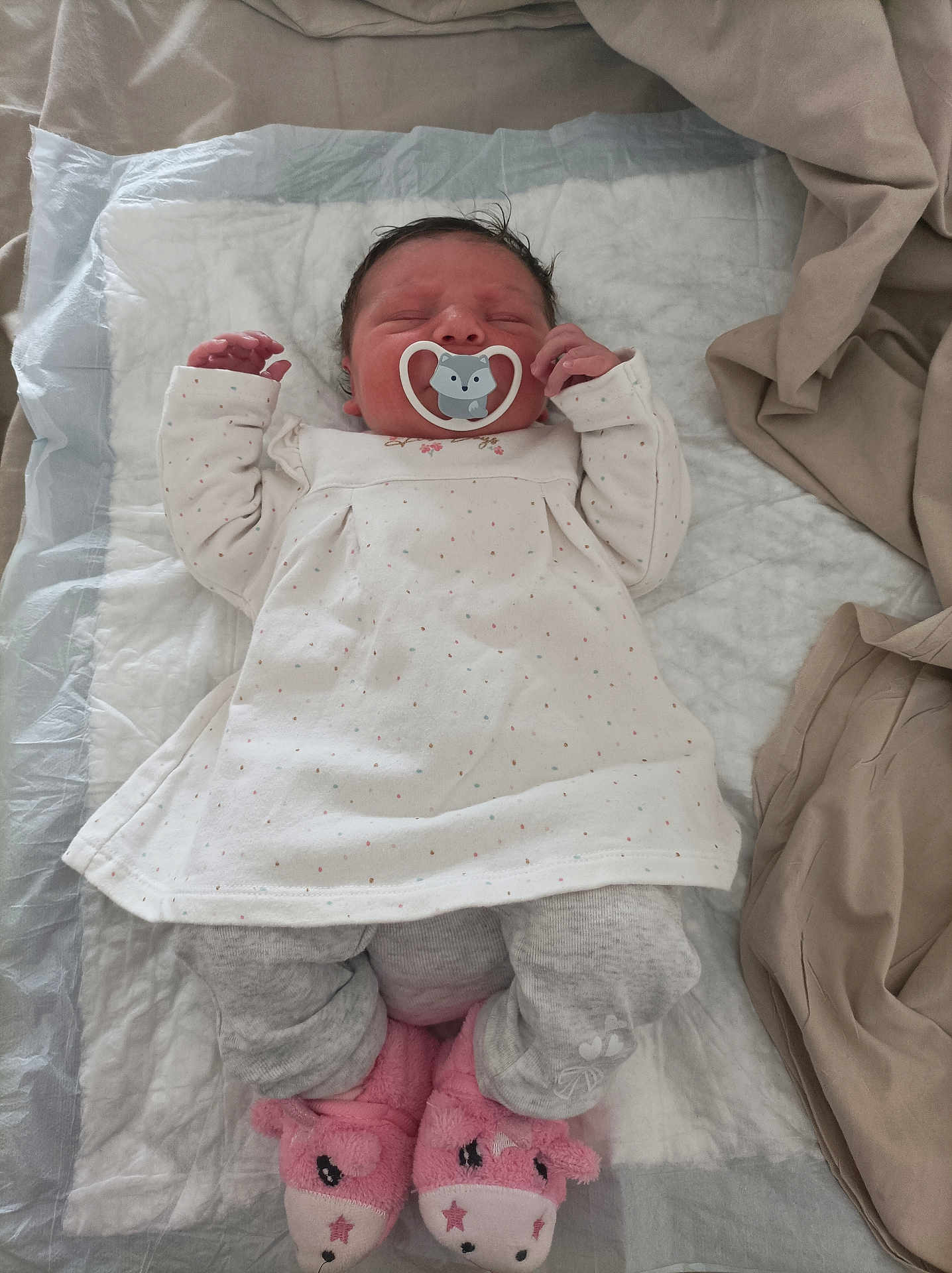 Ambre a rejoint le concours — aidez-le/la à gagner de superbes lots ! baby, newborn, sleeping, pacifier, white_dress, gray_pants, pink_slippers, unicorn_slippers, blanket, bed, infant, person, cute, indoors, soft, resting, child, cozy, sleep, wearing