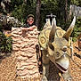child, boy, sunglasses, cap, dinosaur, triceratops, statue, rock, outdoor, sunlight, trees, woodchips, skeleton, t_rex, nature, fun, smile, park, adventure, play