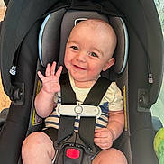 Wesley is registered to the contest to win money with this photo: baby, car_seat, smiling, waving, infant, child, seatbelt, safety_harness, indoor, cute, happy, person, head, face, clothing, striped, skin, arm, leg, toy