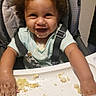 baby, child, high_chair, smiling, eating, food, crumbs, messy, mealtime, portrait, face, curly_hair, infant, sitting, indoors, harness, tray, happy, playful, family