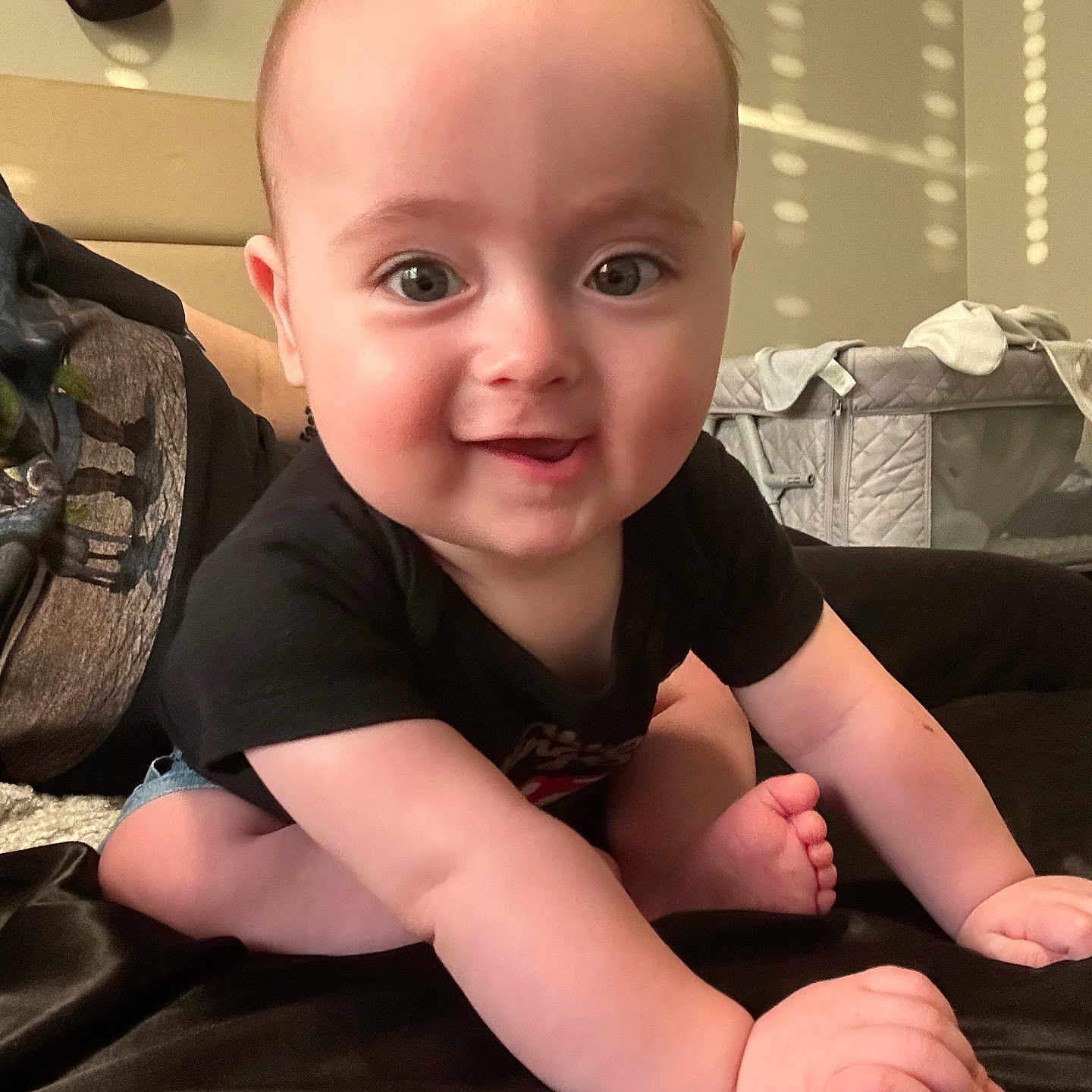 Rowan is registered to the contest to win money with this photo: baby, child, crawling, smiling, black_shirt, denim_shorts, indoors, soft_light, sunlight, wall_pattern, head, face, hands, feet, bedroom, crib, blanket, person, cute, happy